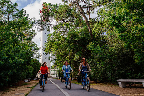 Drie vrouwen fietsen met de vuurtoren van Cap Ferret op de achtergrond.