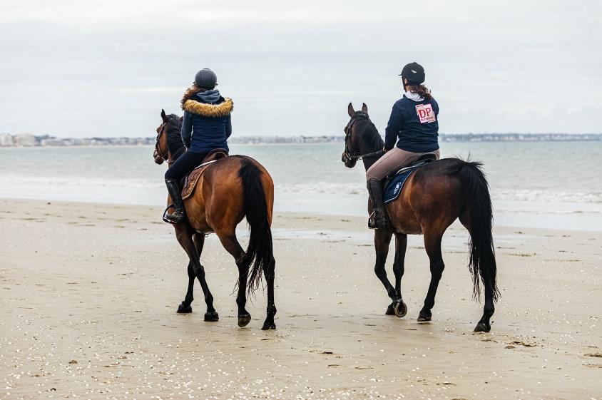Twee mensen rijden te paard over het strand in de Atlantische Kust van Frankrijk.