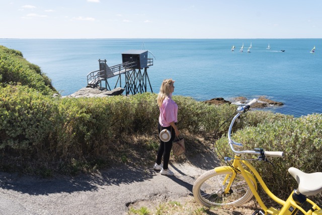 Een mevrouw met een gele fiets kijkt uit over de oceaan in Pornic.